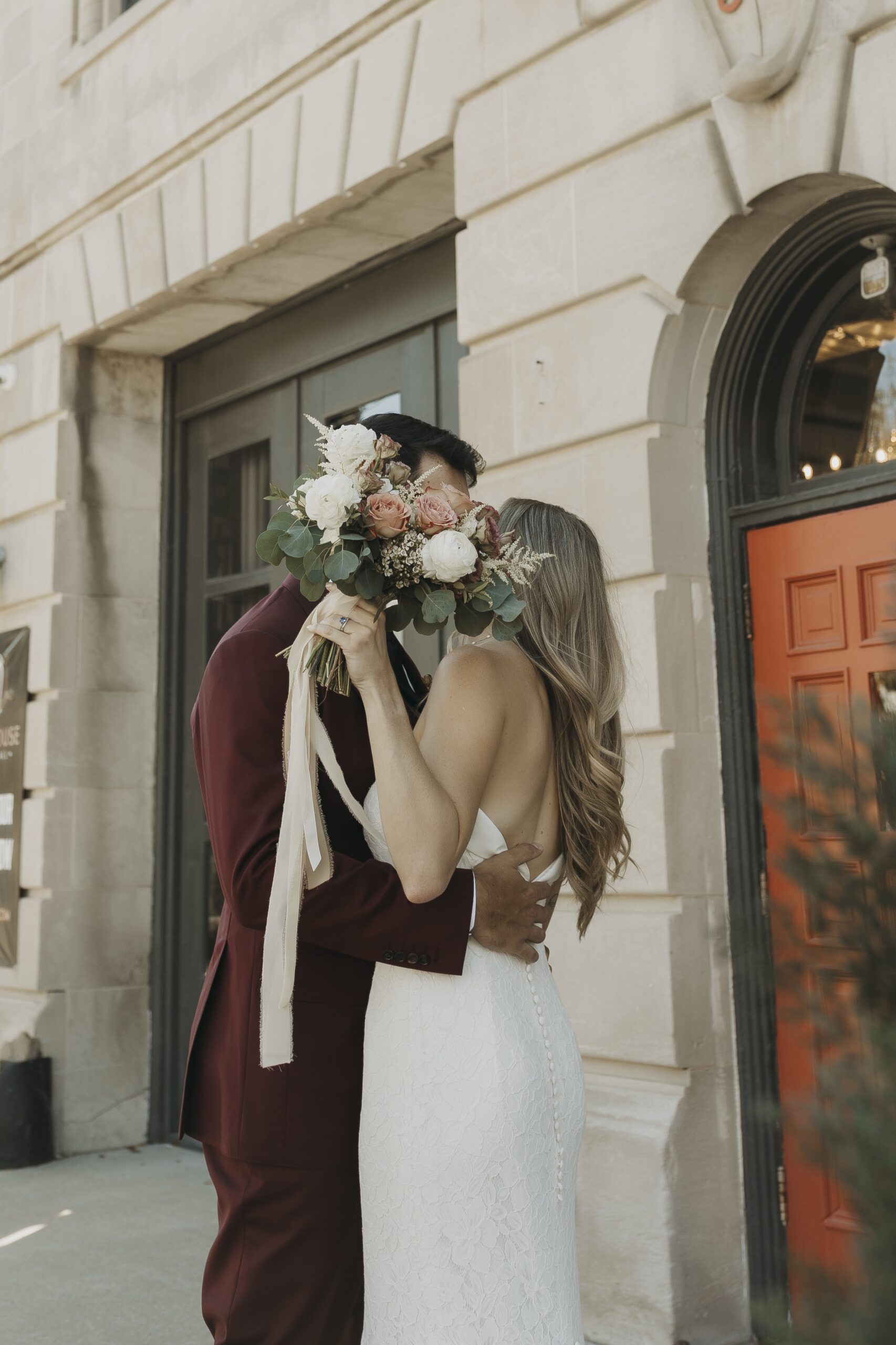 bride and groom kissing behind bouquet